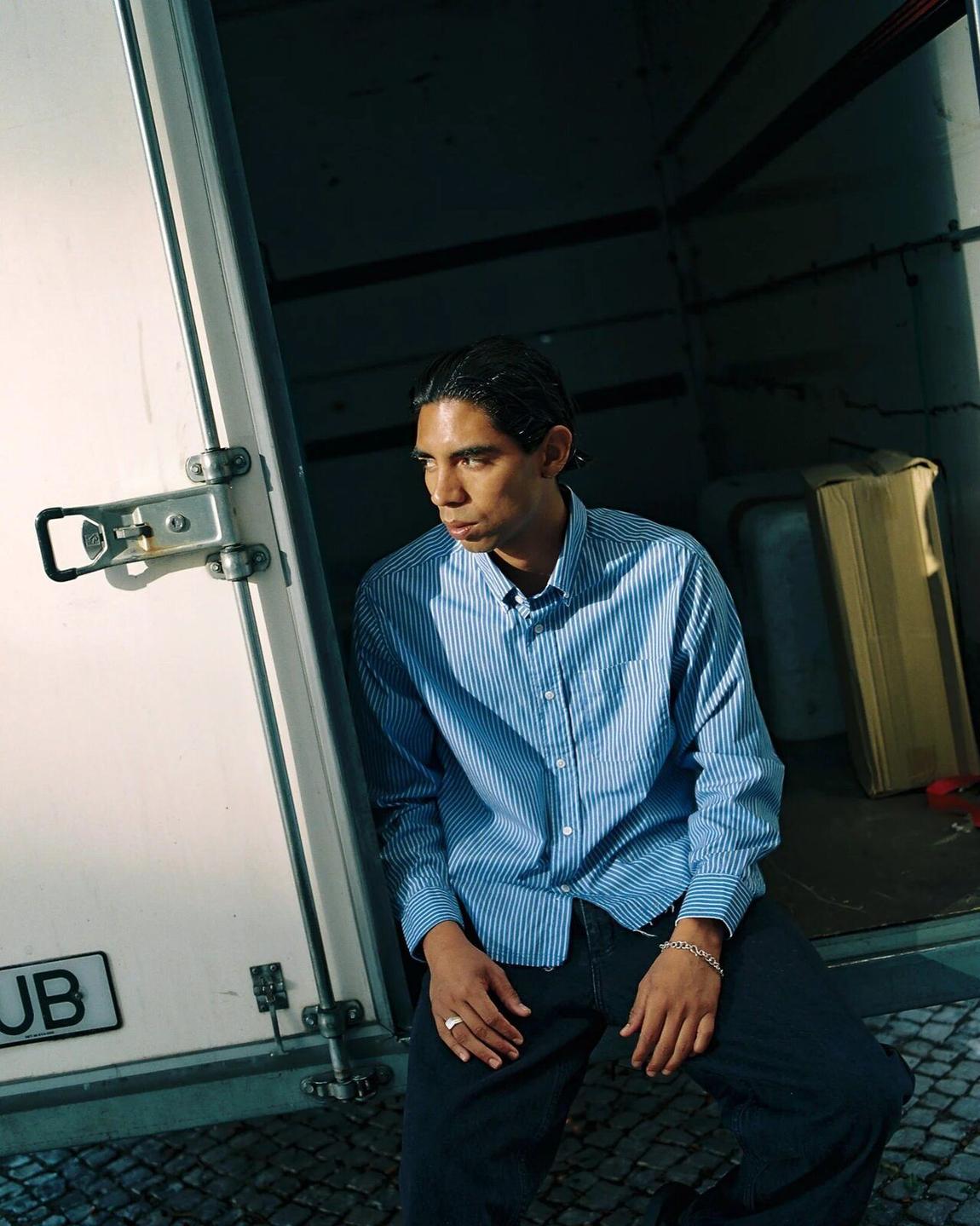 Fairly Normal FW26 campaign: a man in a blue shirt sitting in the back of a van.