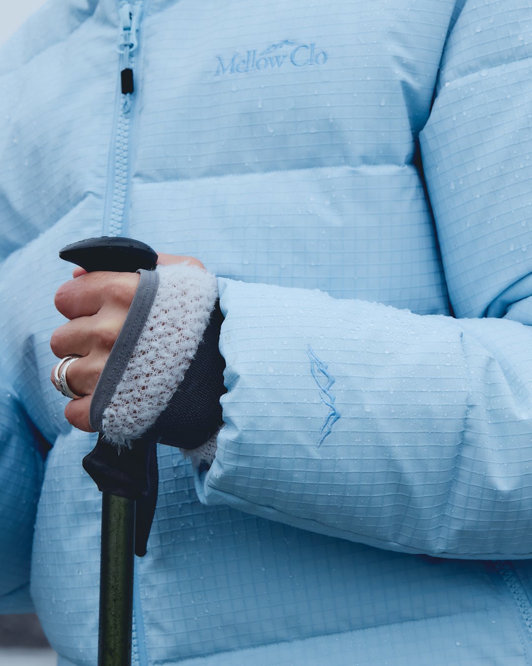A close view of a hand on a walking pole, against a pale blue ripstop down jacket.
