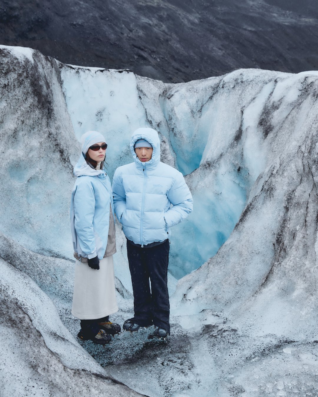 Two people in pale blue down jackets standing in an ice cave.