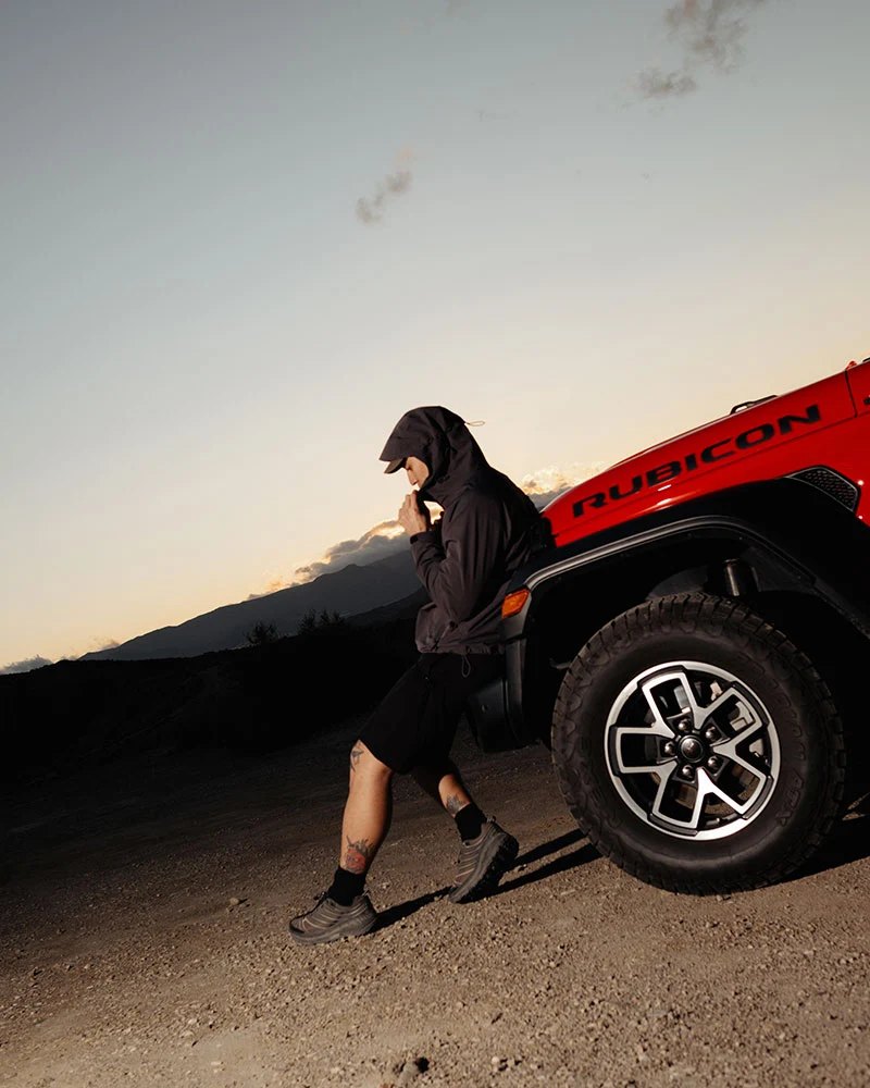 A man in black leaning on the bonnet of a red off-road vehicle at dusk.