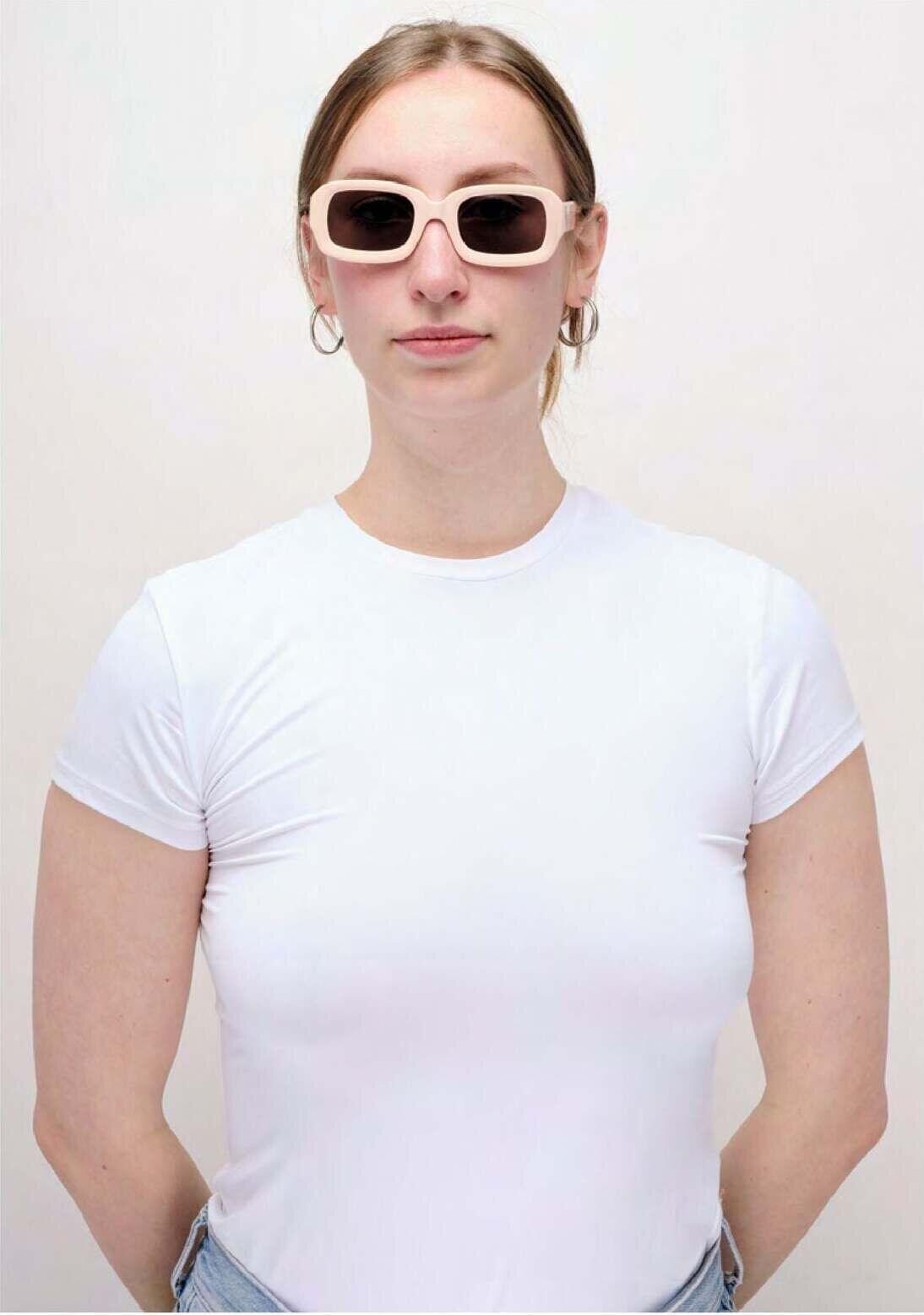 Waiting for the Sun: a woman in a white T-shirt wearing pale rectangular sunglasses.