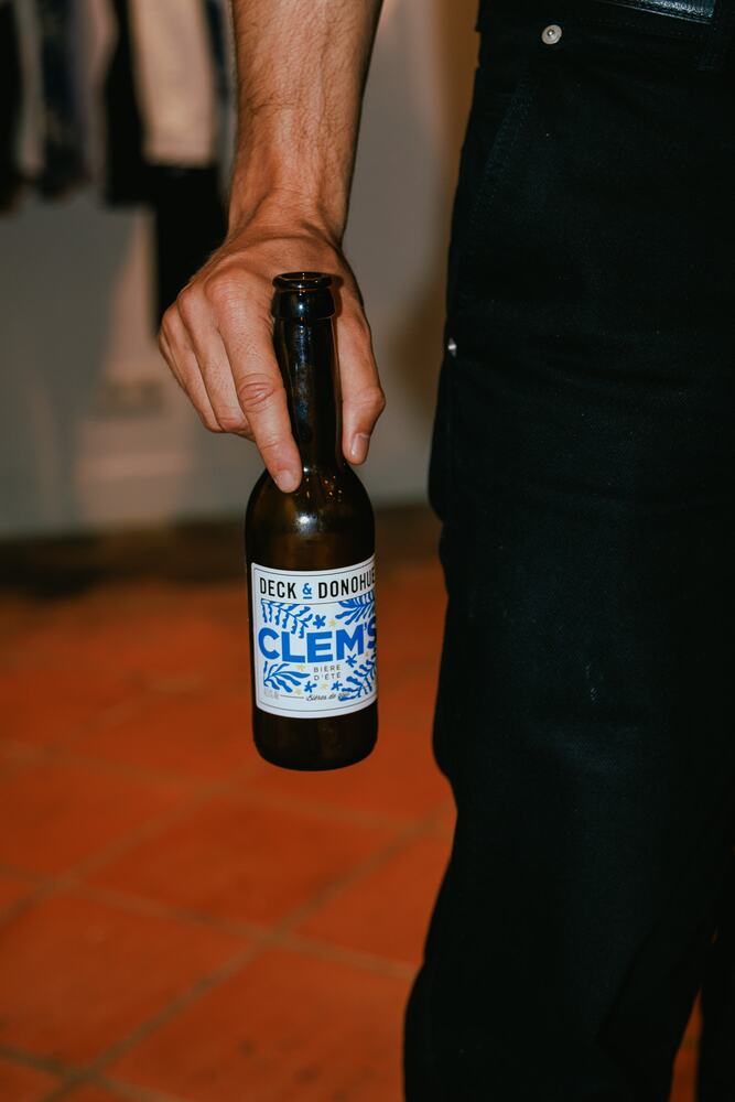 A hand holding a bottle of beer over the terracotta floor.
