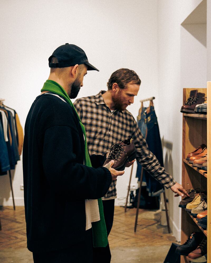 A buyer in a green scarf looking along the shoe shelves with a brand.