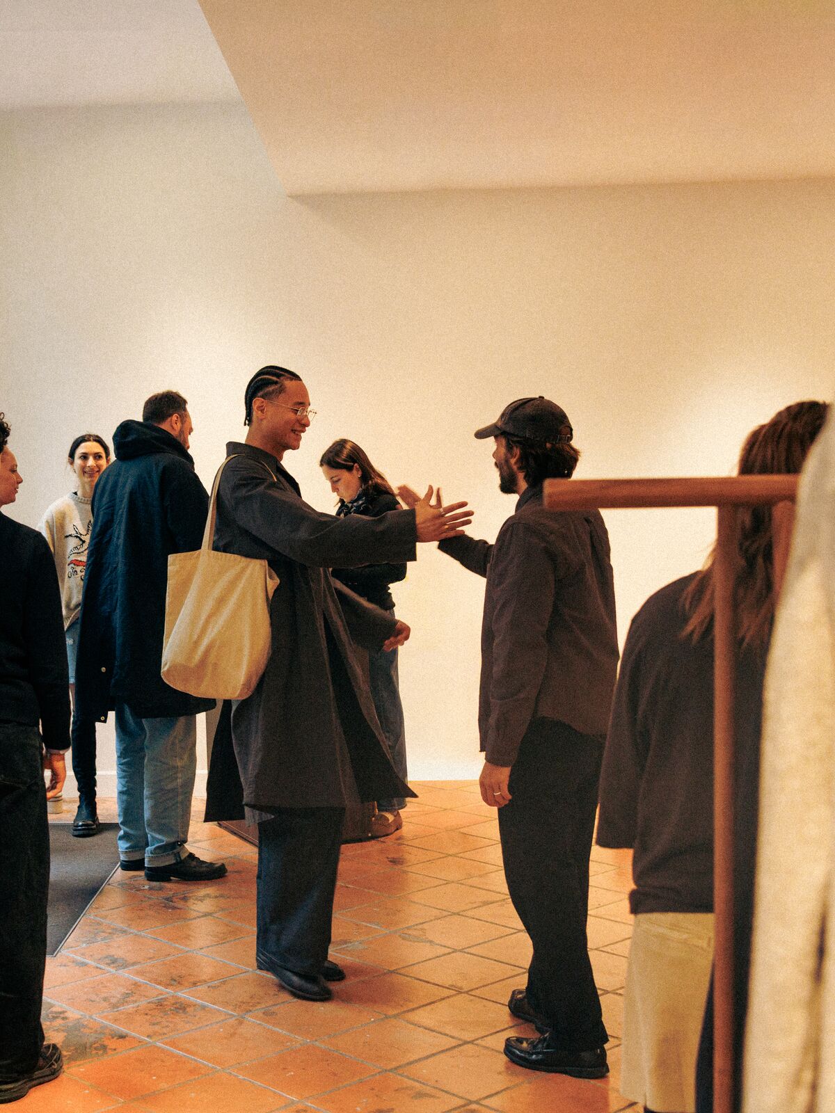 Two visitors greeting each other with open arms in the Paris showroom, on the terracotta floor.