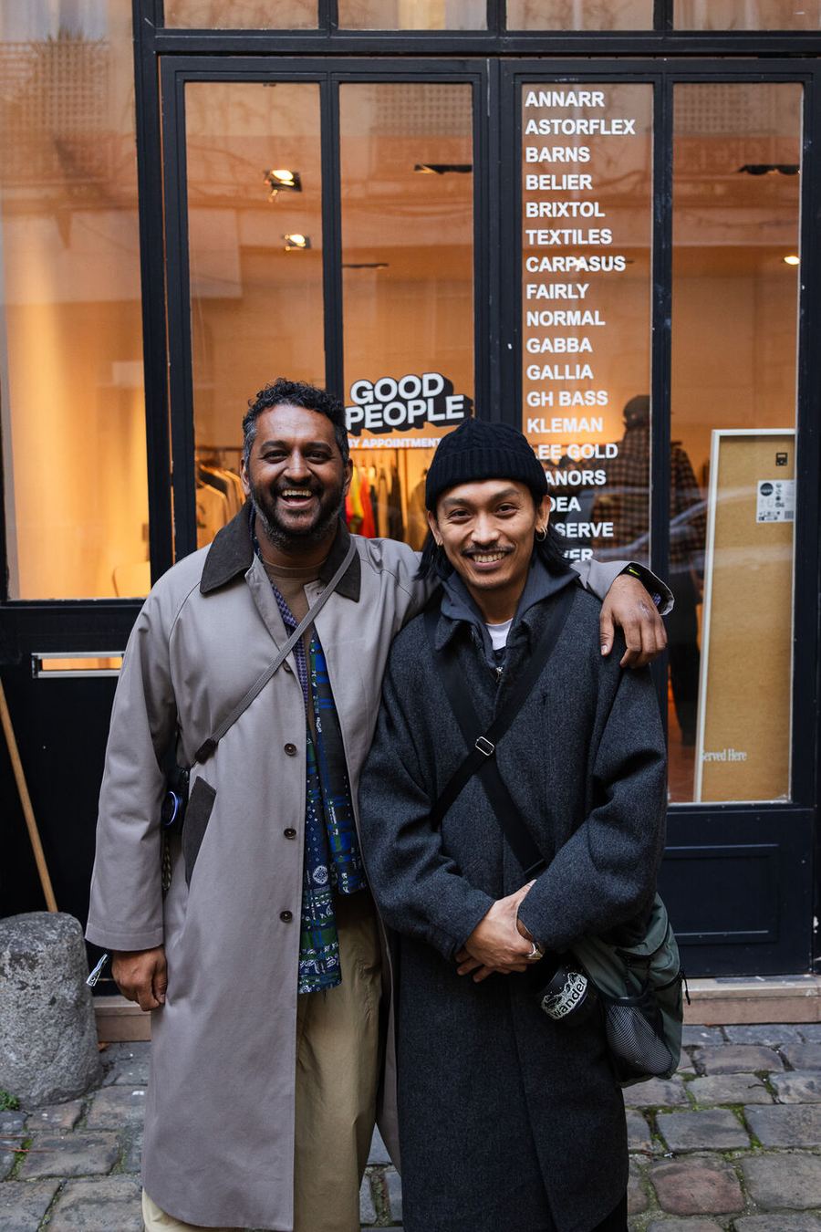 Two visitors smiling outside the Good People showroom window in Paris.